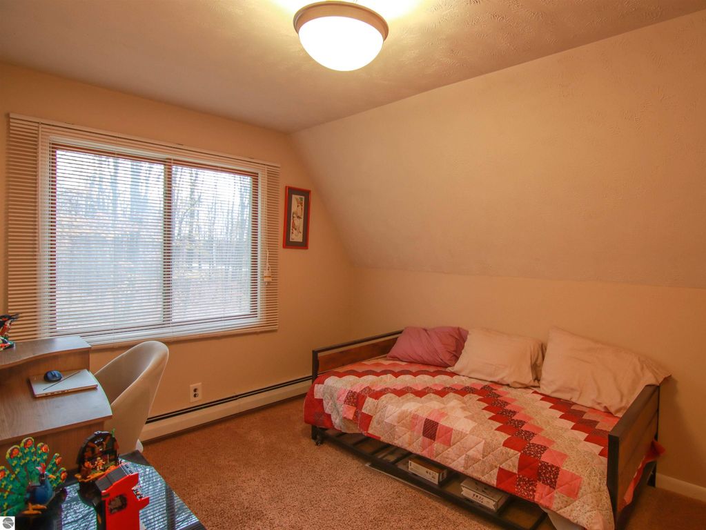 Cozy bedroom featuring a daybed with a colorful quilt, a desk, and large windows overlooking wooded scenery, in a 3-bedroom, 2-bath home for sale in Copemish, MI.