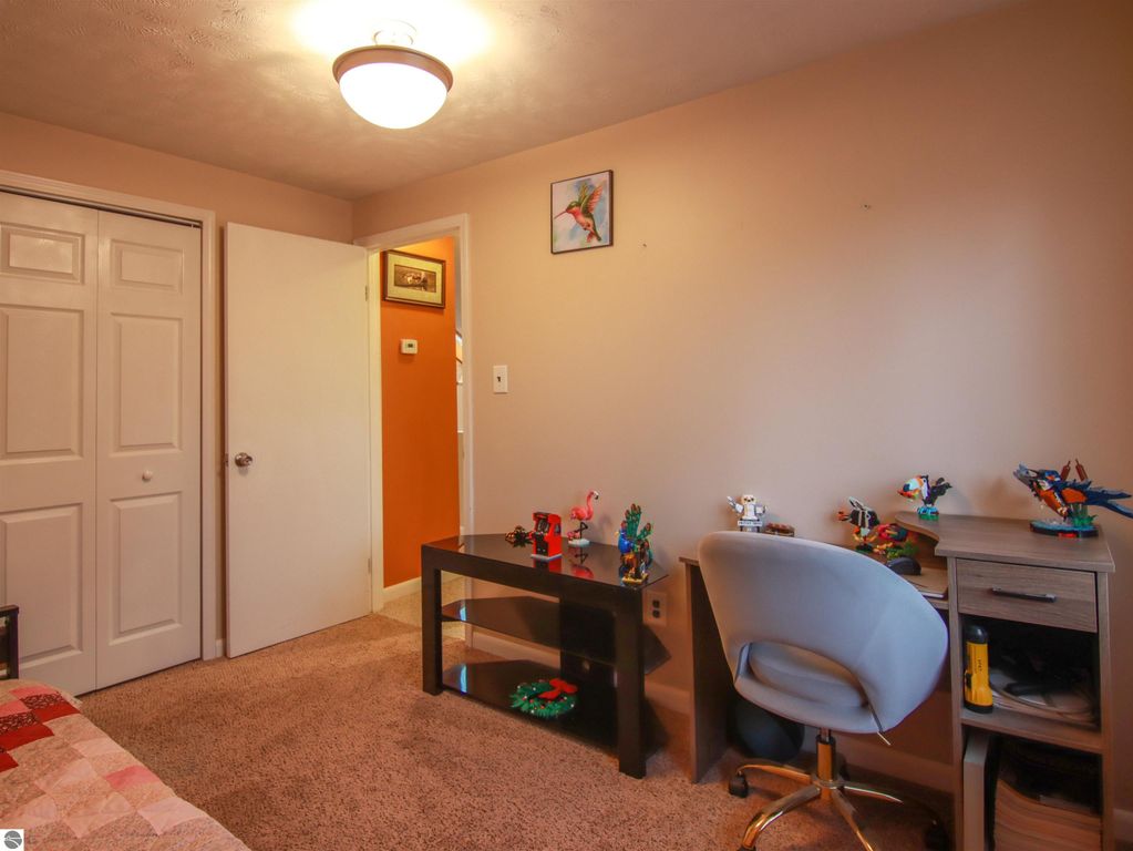 Cozy bedroom featuring a light-colored wall, plush carpet, a desk with toys, and a comfortable chair, showcasing a welcoming atmosphere in a 3-bedroom, 2-bath home for sale in Copemish, MI.