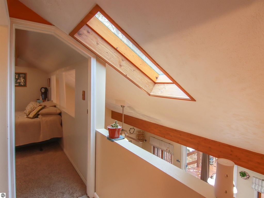 Interior view of a cozy upper hallway in a saltbox style home, featuring a skylight, a bedroom doorway, and decorative elements, highlighting the inviting atmosphere of the 3-bedroom, 2-bathroom property for sale in Copemish, MI.