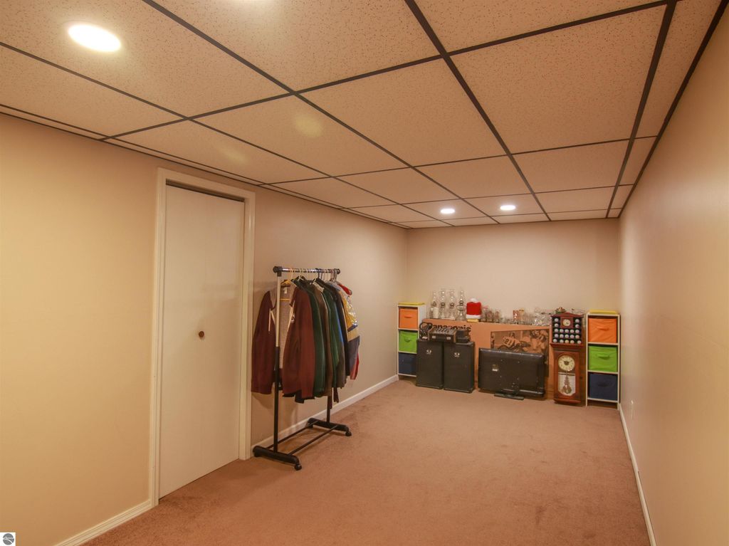 Finished lower level room with beige walls, carpeted floor, clothing rack, storage units, and various decorative items, suitable for media or hobby space in a 3-bedroom, 2-bath home in Copemish, MI.