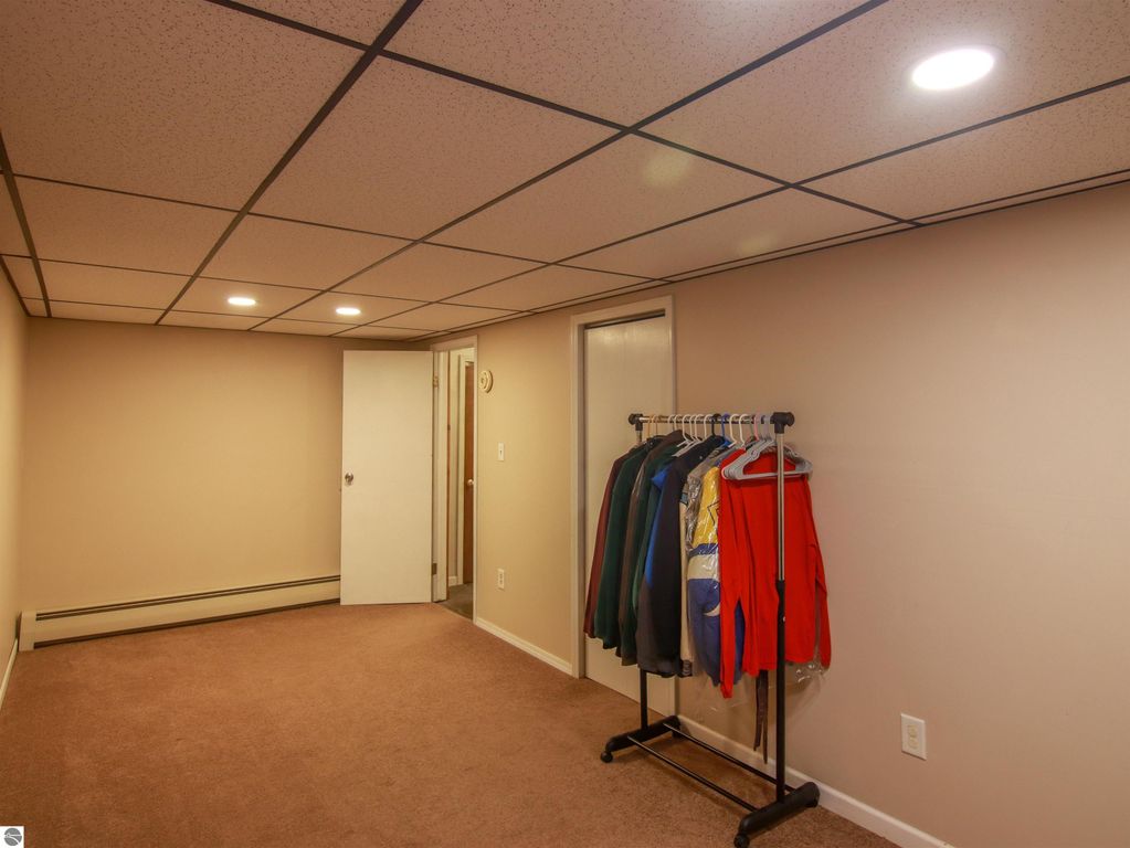 Finished lower level room with carpet, closet space, and clothing rack, suitable for media or hobby use, in a 3-bedroom home at 20280 Cadillac Highway, Copemish, MI.