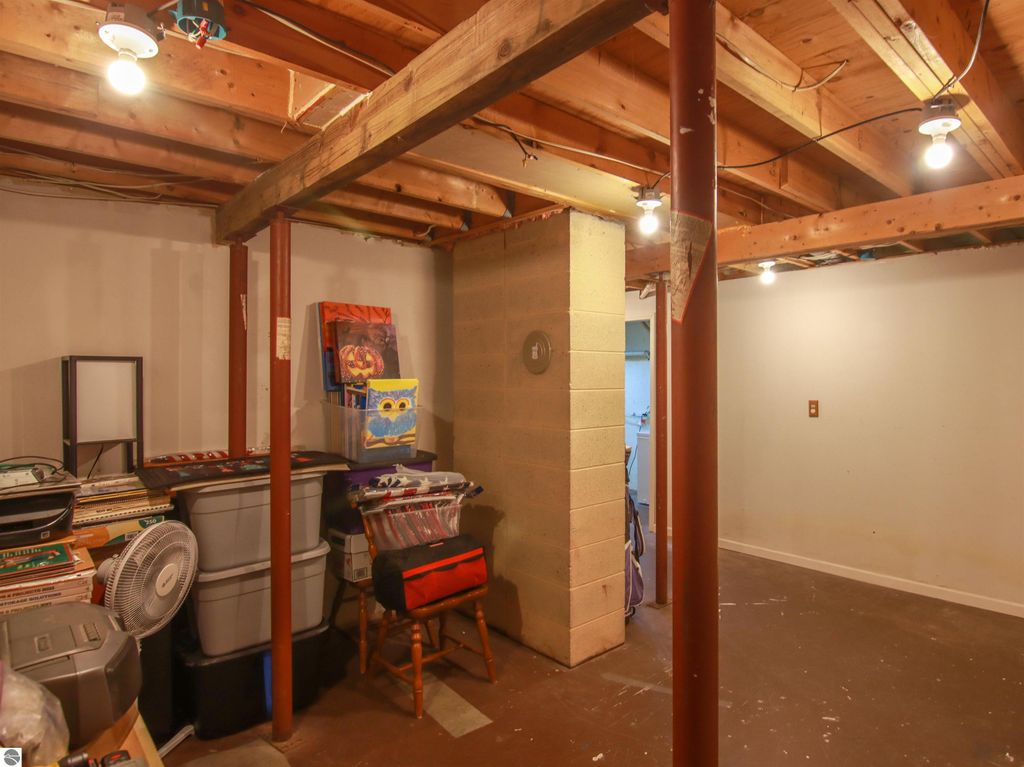 Basement storage area with organized bins, shelves, and a wooden support beam, showcasing potential for media room or hobby space in the 3-bedroom home at 20280 Cadillac Highway, Copemish, MI.