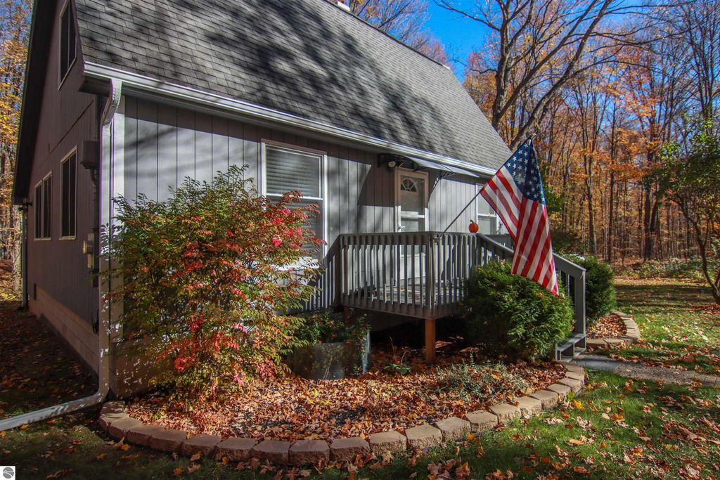 Saltbox style home at 20280 Cadillac Highway, surrounded by autumn foliage, featuring a welcoming porch with an American flag, landscaped yard, and wooded backdrop.