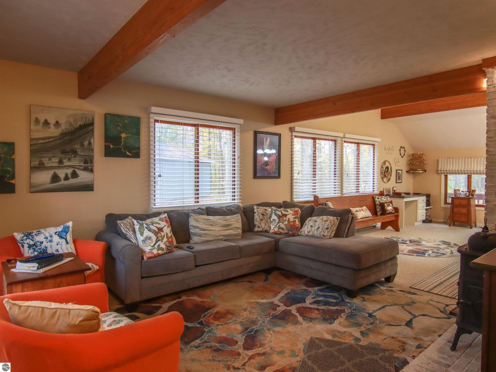 Cozy living room in a saltbox style home featuring a sectional sofa, decorative pillows, and artwork on walls, with large windows providing natural light and views of the surrounding woods.