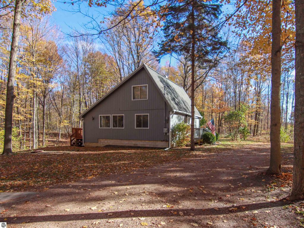 3-bedroom, 2-bathroom saltbox home on 8.75 acres in Copemish, MI, featuring a welcoming exterior, surrounded by autumn foliage and a gravel driveway.