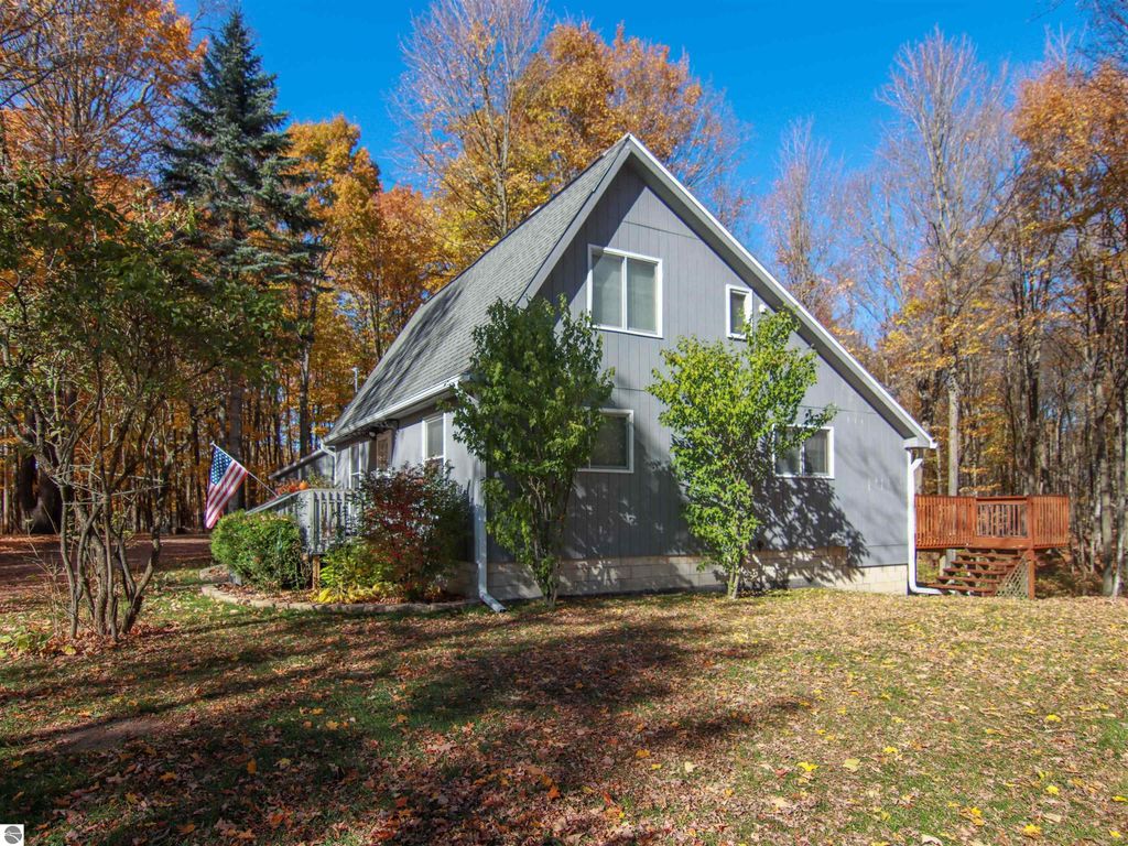 Saltbox style home at 20280 Cadillac Highway, Copemish, MI, featuring autumn foliage, American flag, and spacious yard with deck, ideal for serene living on 8.75 acres.