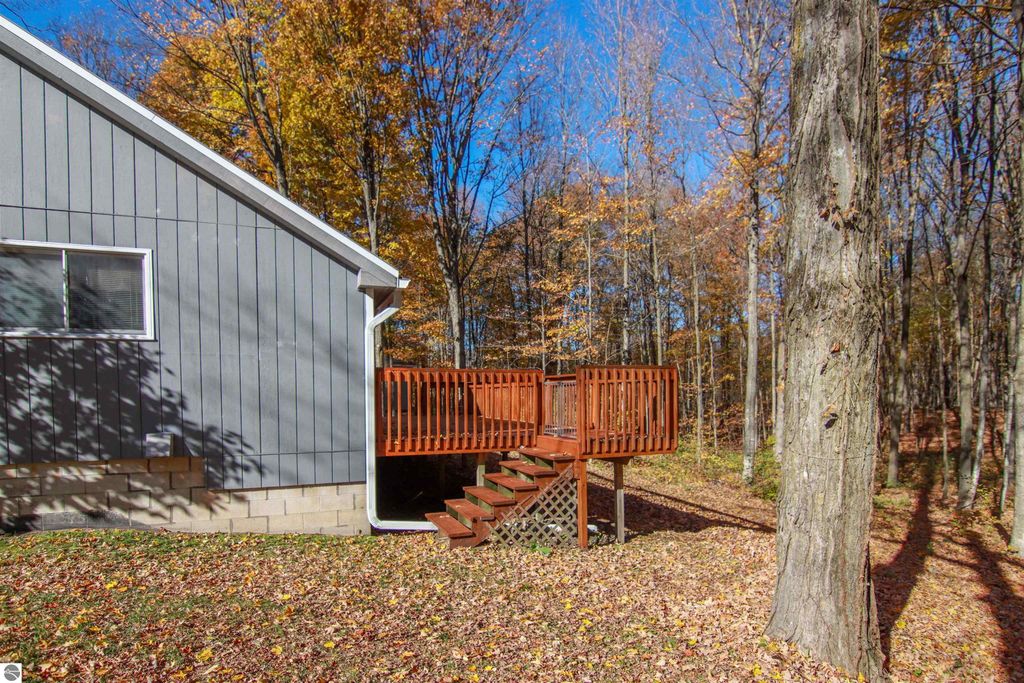 Side view of a saltbox-style home with a wooden deck, surrounded by autumn foliage, showcasing the natural setting and outdoor space in Copemish, MI.