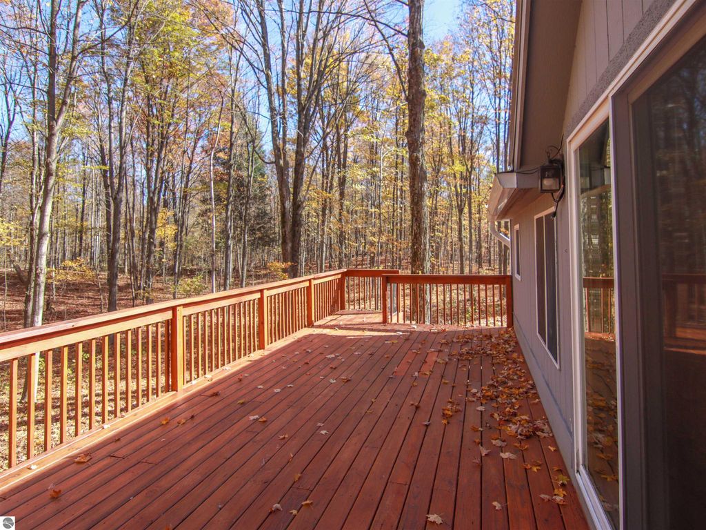 Spacious wooden deck overlooking wooded landscape, showcasing autumn foliage, part of a 3-bedroom, 2-bathroom home in Copemish, MI.