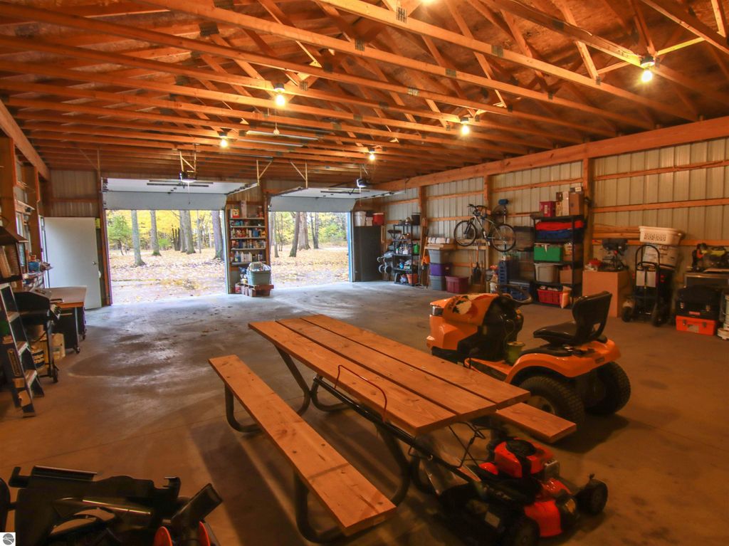 Spacious 30x40 detached pole barn garage with picnic table, storage shelves, and tools, featuring two garage doors opening to wooded views.