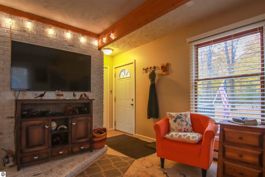 Welcoming interior of a 3-bedroom, 2-bathroom home featuring a cozy living area with a mounted TV, decorative wooden cabinet, orange armchair, and an entrance door, highlighting the inviting atmosphere of the property at 20280 Cadillac Highway, Copemish, MI.