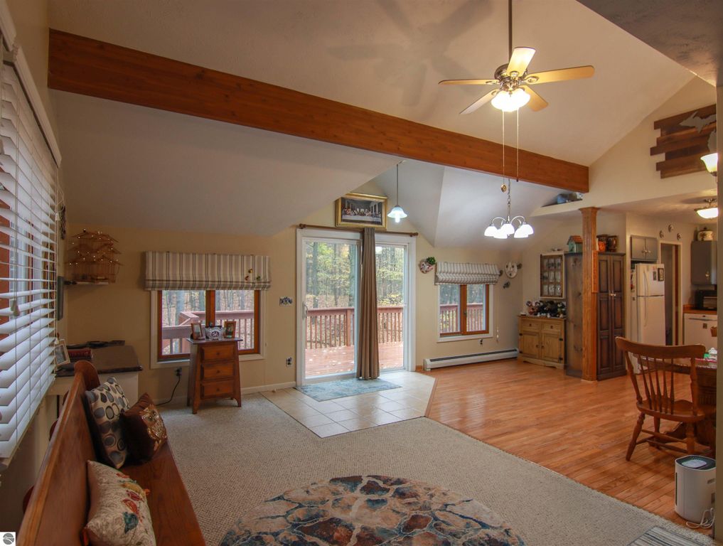 Welcoming interior of a 3-bedroom, 2-bath saltbox home featuring a woodstove, open living space, and access to a sunlit deck overlooking wooded hills, highlighting cozy furnishings and rustic decor.
