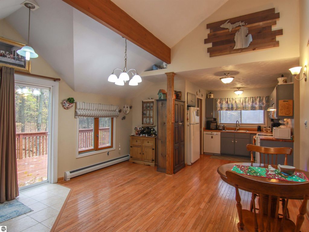 Welcoming interior of a 3-bedroom, 2-bathroom saltbox home featuring a woodstove, sunlit kitchen, and dining area, with a view of the deck and wooded surroundings.