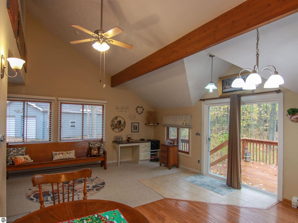 Welcoming interior of a saltbox style home featuring a woodstove, dining area, and large windows overlooking wooded views, highlighting the inviting living space and access to a rear deck.