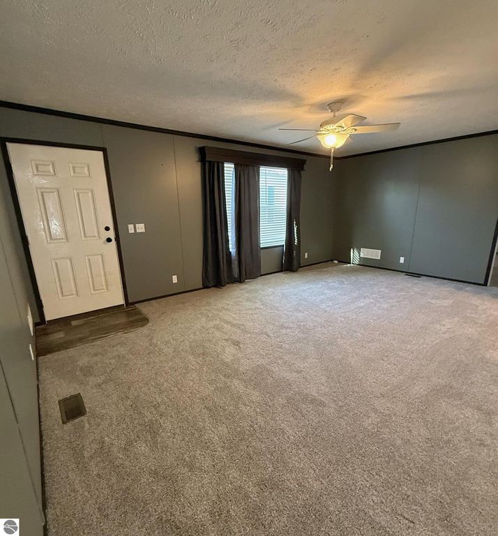 Spacious living room with gray walls, carpeted flooring, ceiling fan, and large windows with curtains, showcasing a welcoming interior of the home at 1032 Pebble Creek, Mt Pleasant, MI.