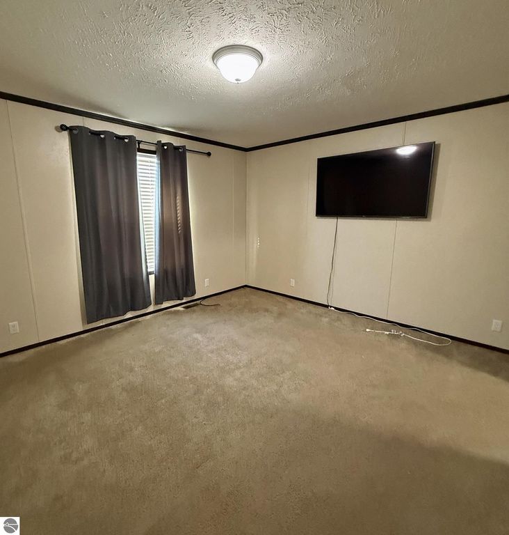 Cozy living room in a 3-bedroom home at 1032 Pebble Creek, featuring gray curtains, a wall-mounted TV, and plush carpeting, highlighting comfort and charm in the Summerhill Village community.