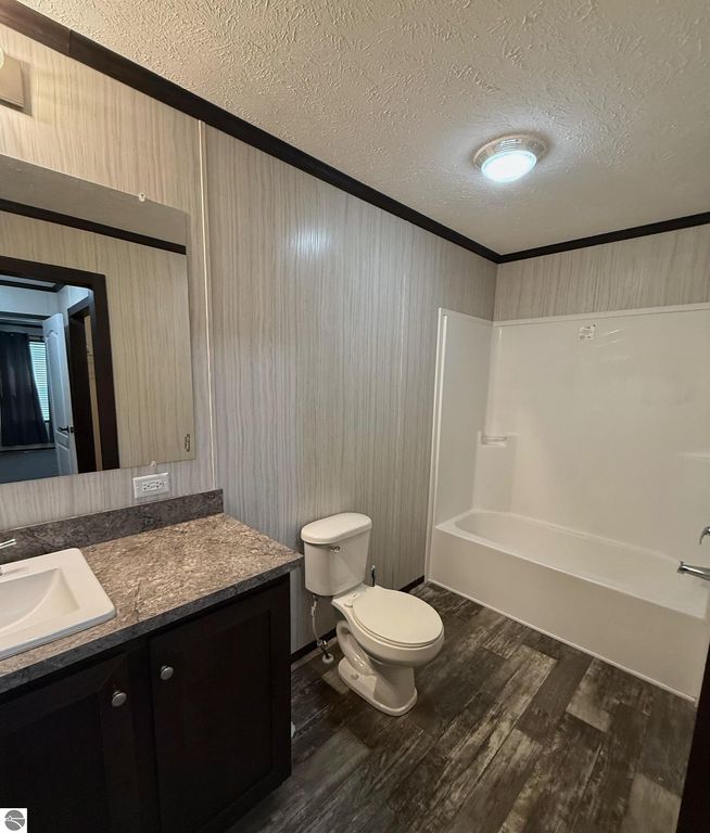 Modern bathroom featuring a granite countertop sink, toilet, and a shower-tub combination, with stylish wall paneling and natural light from an adjacent room.