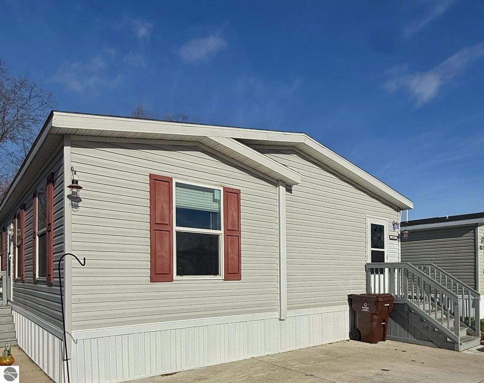 Exterior view of a single-family home at 1032 Pebble Creek, featuring beige siding, red shutters, and a front porch with steps, situated in a peaceful community in Mt Pleasant, MI.
