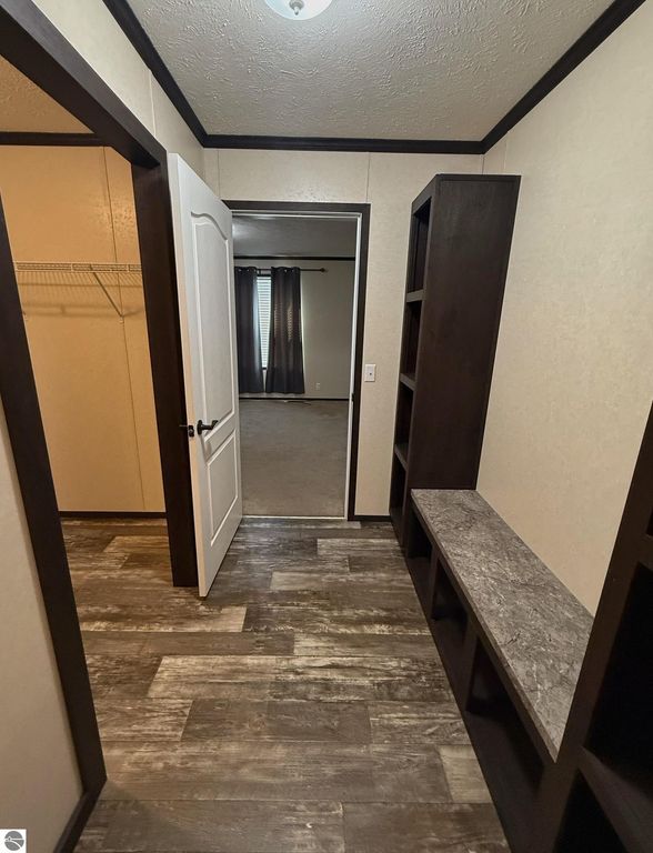 Interior hallway of a home featuring a white door leading to a room, dark wood shelves, and a closet with a wire rack, showcasing modern flooring and a well-lit space.