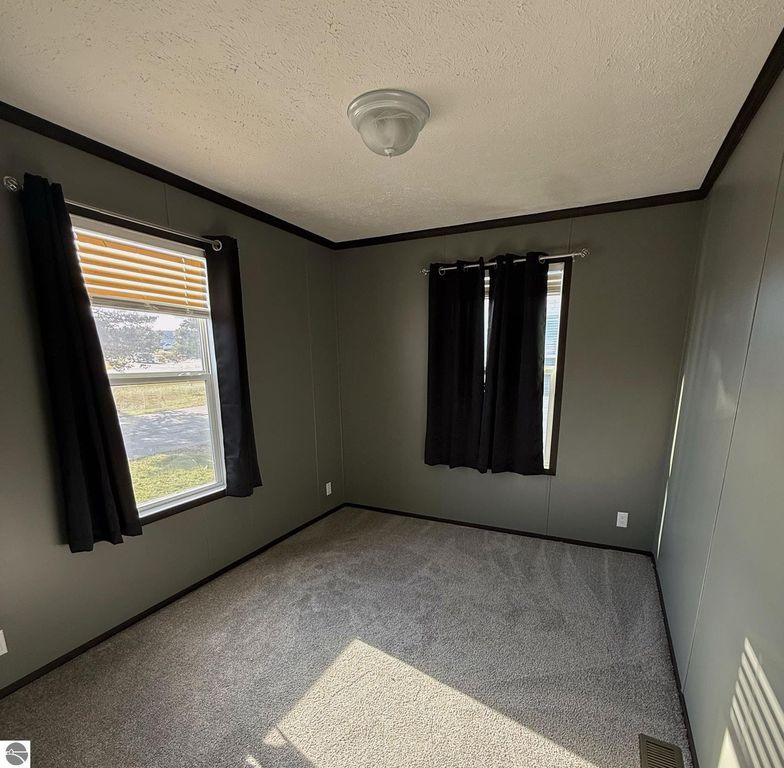 Cozy interior of a bedroom featuring gray walls, plush carpet, two windows with blinds, and black curtains, showcasing natural light in a home for sale at 1032 Pebble Creek, Mt Pleasant, MI.