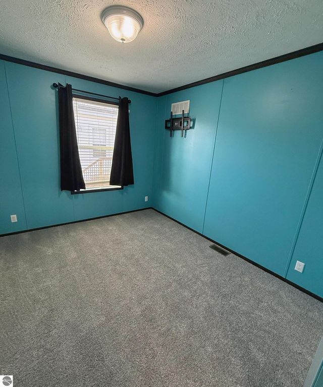 Interior view of a freshly painted bedroom with teal walls and gray carpet, featuring a window with black curtains and a wall-mounted bracket, showcasing the charm and comfort of the home at 1032 Pebble Creek, Mt Pleasant, MI.