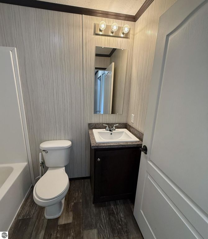 Modern bathroom interior featuring a toilet, sink with a dark cabinet, and a mirror, showcasing updated fixtures and stylish wall paneling.