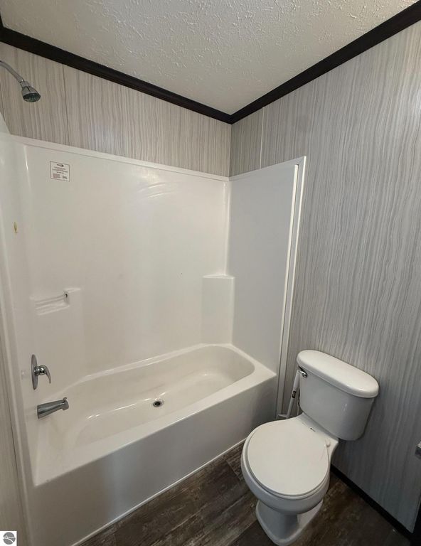 Bathroom interior featuring a white bathtub with showerhead, adjacent to a modern toilet, and textured wall design, showcasing the updated amenities of the home at 1032 Pebble Creek, Mt Pleasant, MI.