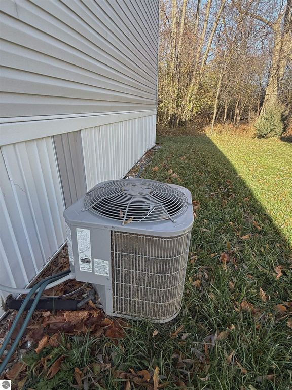 Air conditioning unit beside house exterior, surrounded by grass and autumn leaves, showcasing the property's outdoor features at 1032 Pebble Creek, Mt Pleasant, MI.