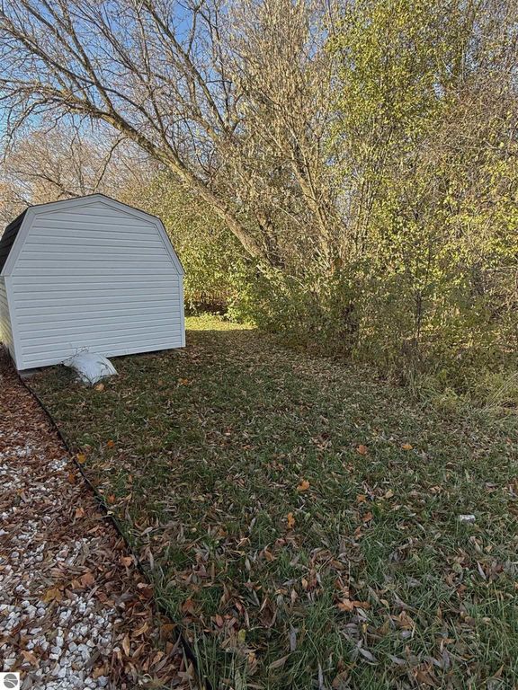 White shed in a serene backyard surrounded by trees and grass, featuring a peaceful natural setting ideal for a home at 1032 Pebble Creek, Mt Pleasant, MI.
