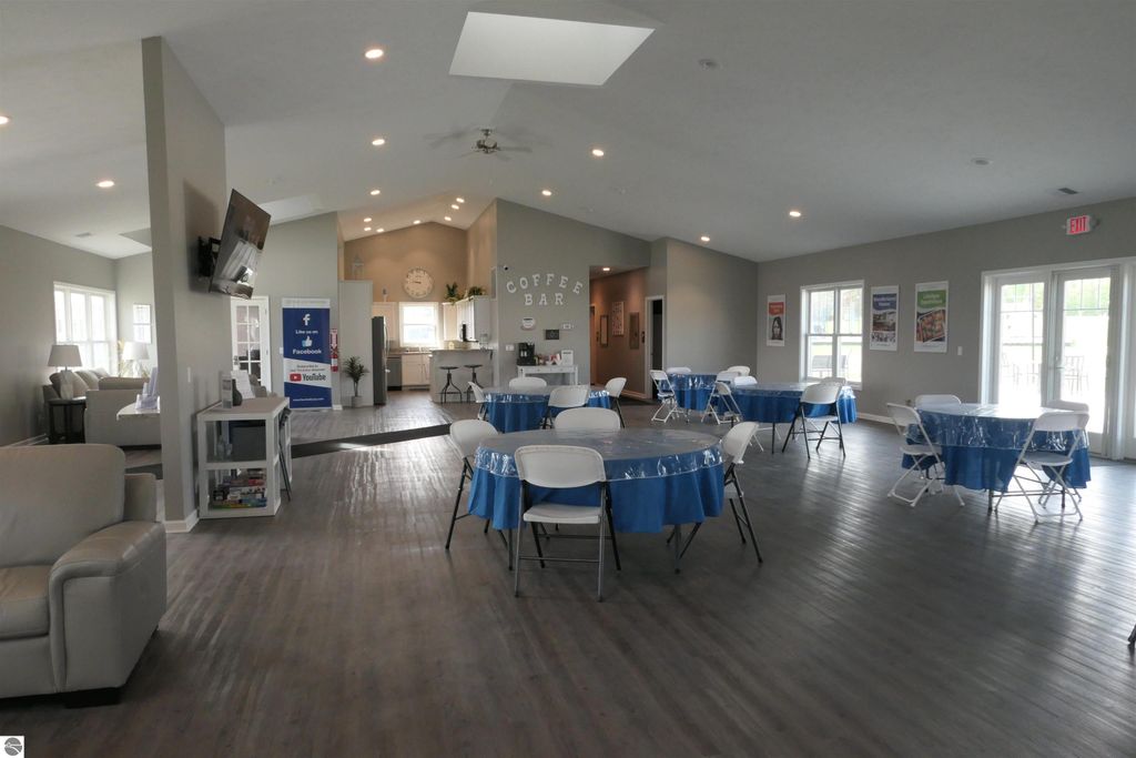 Community clubhouse interior featuring multiple round tables with blue tablecloths, a coffee bar area, and a cozy seating arrangement, ideal for gatherings and events in Summerhill Village, Mt Pleasant, MI.