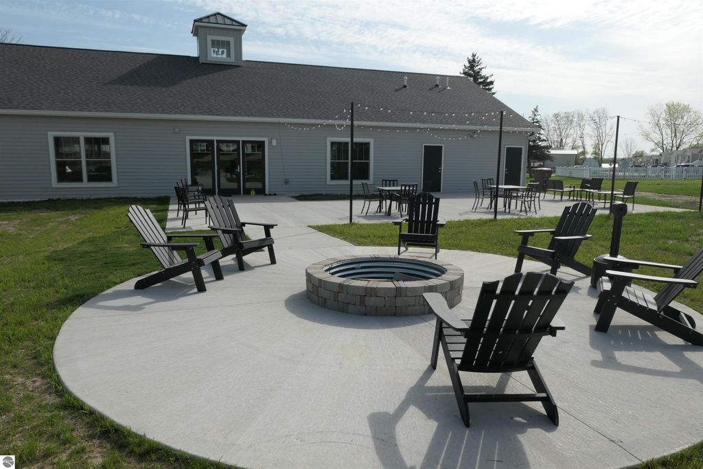 Outdoor community space at Summerhill Village featuring a fire pit surrounded by black Adirondack chairs, with a clubhouse in the background and green lawn area.