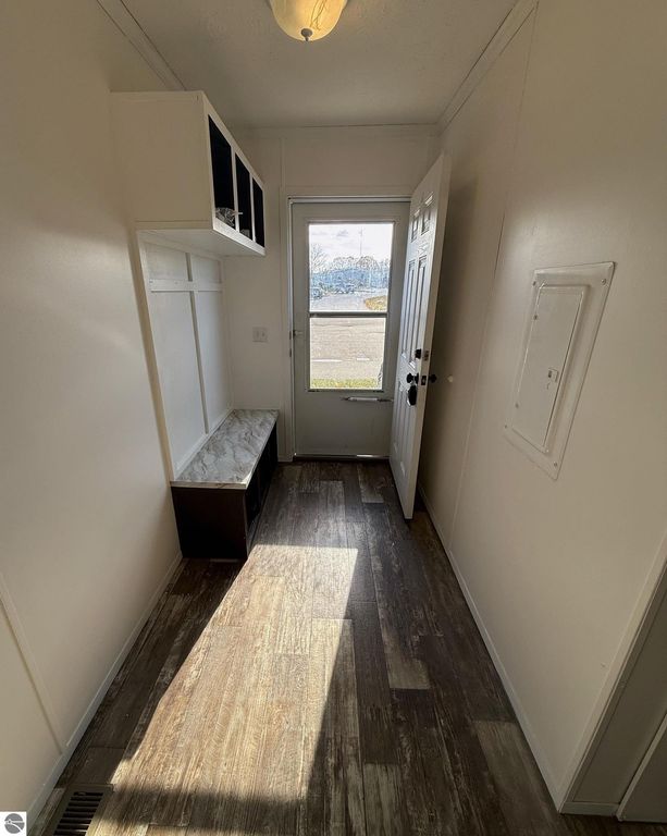 Interior entryway of a home featuring a bench with storage, white walls, a door leading outside, and a light fixture, emphasizing comfort and convenience in the listing for 1032 Pebble Creek, Mt Pleasant, MI.
