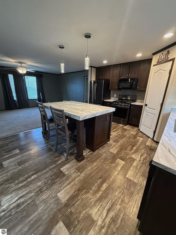 Modern kitchen with dark cabinetry, granite island, stainless steel appliances, and open layout towards living area in a 3-bedroom home at 1032 Pebble Creek, Mt Pleasant, MI.