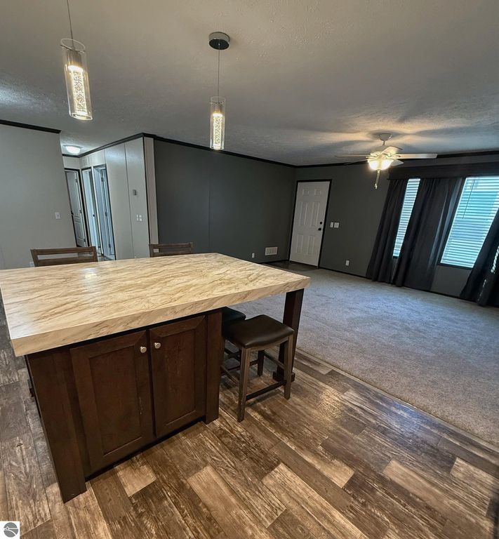 Modern kitchen island with marble countertop and dark wood cabinetry, overlooking spacious living area with ceiling fan and large windows, showcasing comfortable and inviting home atmosphere in Mt Pleasant, MI.