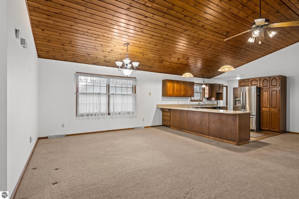 Open concept living area featuring a spacious kitchen with wooden cabinetry, granite countertops, and a large island, complemented by knotty pine ceiling and natural light from multiple windows, ideal for entertaining in the Cadillac, MI home.