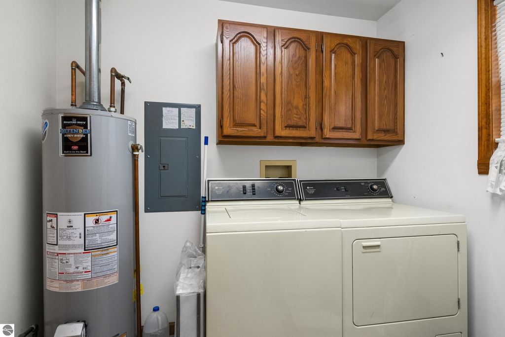 Laundry room featuring a washer and dryer, water heater, electrical panel, and wooden cabinets in a residential home at 396 Davenport Lane, Cadillac, MI.