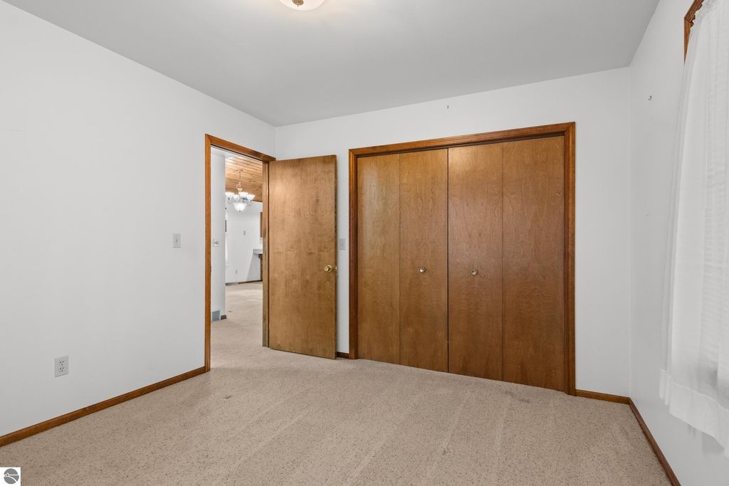 Interior view of a bedroom featuring beige carpet, white walls, and wooden closet doors, with an open doorway leading to another room, showcasing the spacious layout of the home at 396 Davenport Lane, Cadillac, MI.