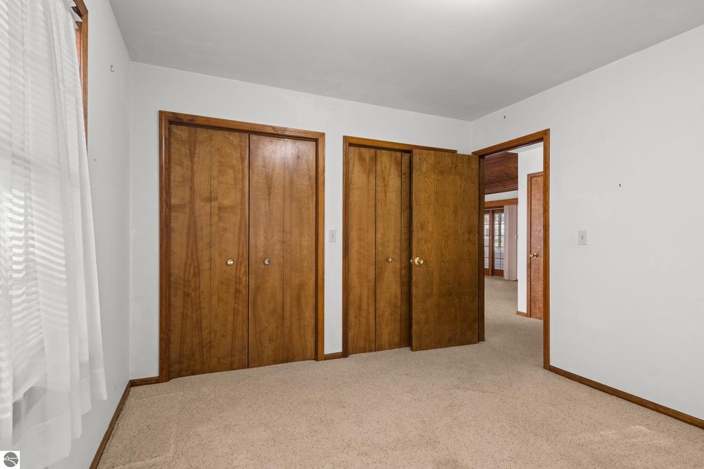 Interior view of a bedroom featuring wooden closet doors, beige carpet, and white walls, showcasing a spacious layout in the home for sale at 396 Davenport Lane, Cadillac, MI.