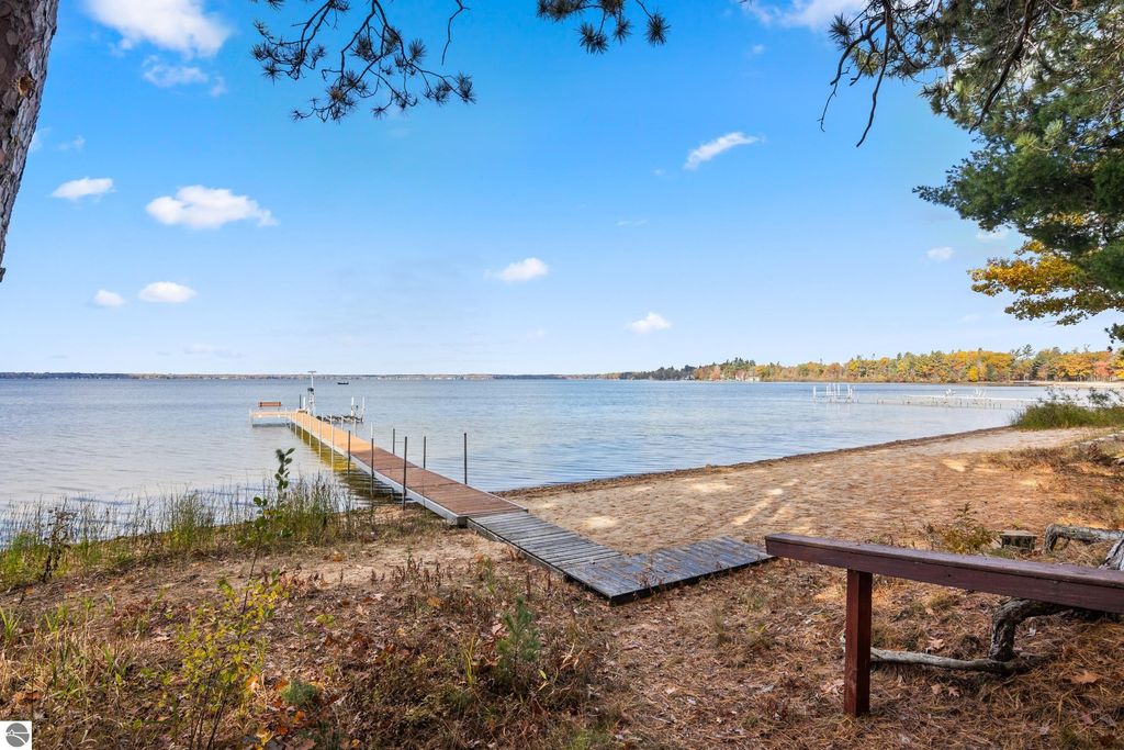 Scenic view of Lake Mitchell with a wooden dock extending into the water, surrounded by a sandy beach and autumn foliage, showcasing the tranquil setting of the property at 396 Davenport Lane, Cadillac, MI.