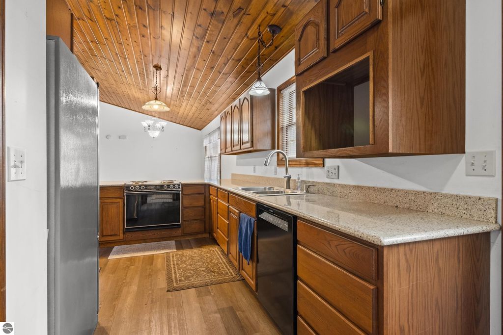 Kitchen interior featuring wooden cabinets, granite countertops, stainless steel appliances, and a knotty pine ceiling, highlighting the spacious design ideal for entertaining in a Cadillac home.