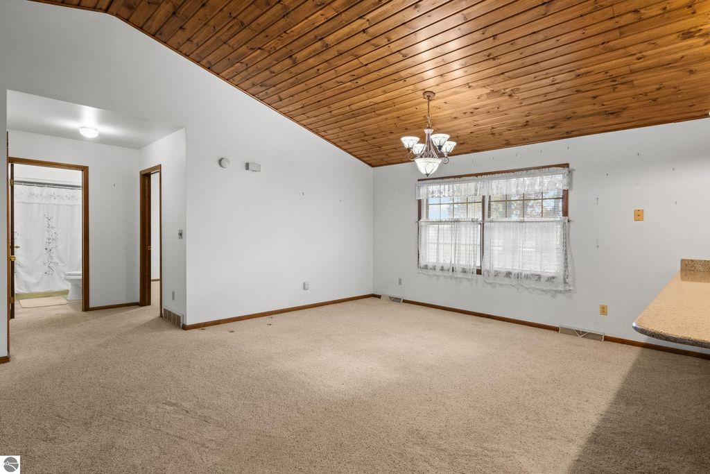 Spacious living area with knotty pine ceiling, large windows, and carpet, showcasing the open floor plan of the 3-bedroom, 2-bath home at 396 Davenport Lane, Cadillac, MI.