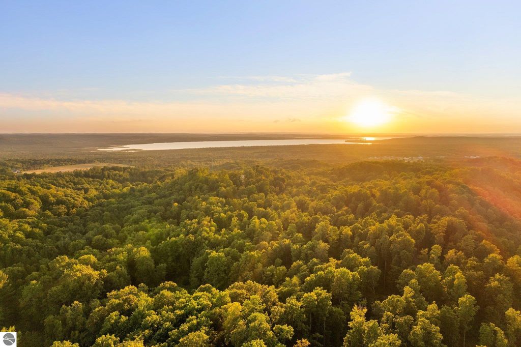 Aerial view of lush green landscape with rolling hills and a sunset over a lake, showcasing the natural beauty of Northern Michigan near Rapid City.