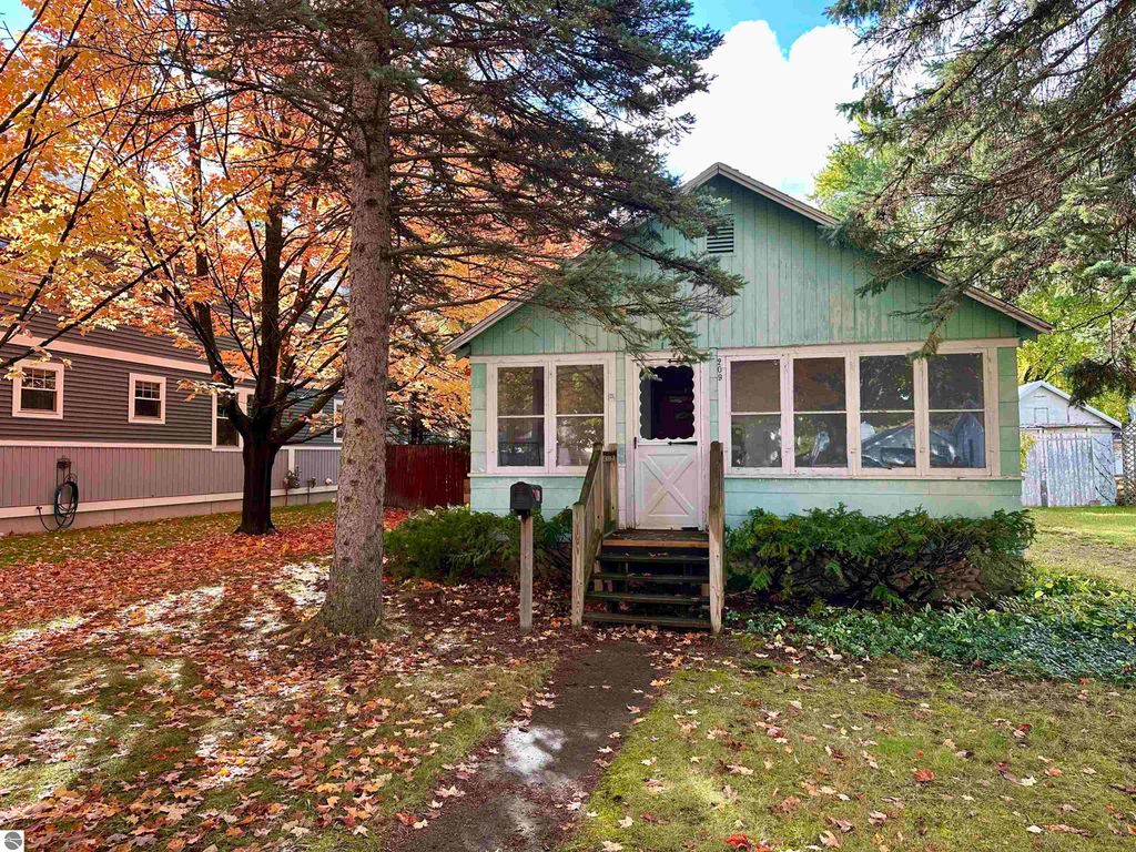 Charming light blue home with enclosed front porch, surrounded by autumn foliage on tree-lined 15th Street in Traverse City, MI, showcasing a welcoming exterior and well-maintained landscaping.