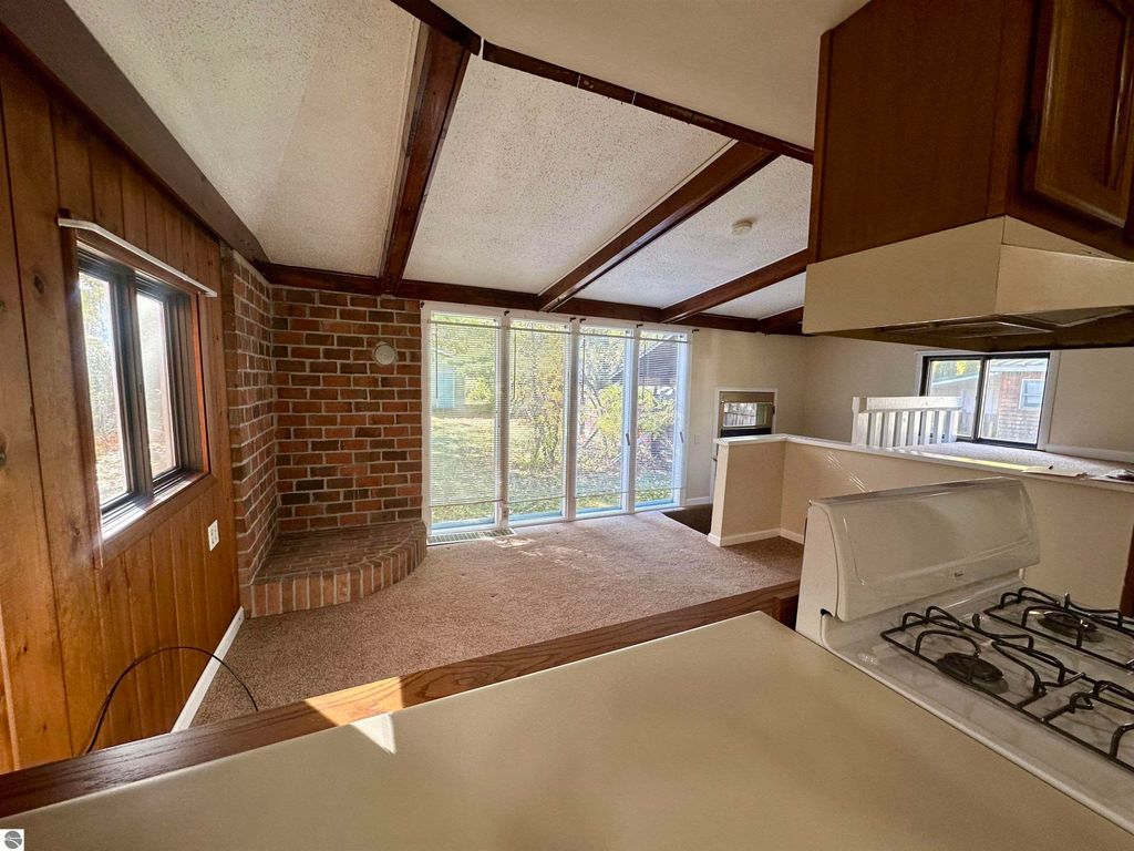 Cozy interior of a home at 209 W Fifteenth Street, Traverse City, featuring a brick accent wall, large windows, and an open layout connecting the kitchen and living area.