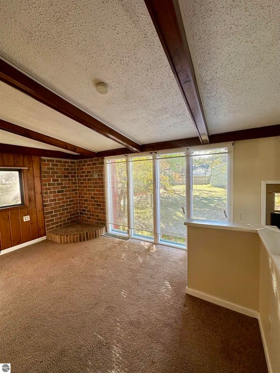 Cozy interior of a one-bedroom home in Traverse City, featuring exposed wooden beams, a brick accent wall, and large windows providing natural light, ideal for showcasing the property's inviting atmosphere.