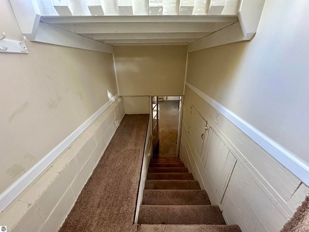 Staircase leading to a basement with carpeted steps and light-colored walls, showcasing the clean and dry interior of the property at 209 W Fifteenth Street, Traverse City, MI.