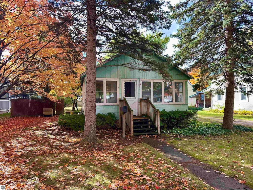 Charming green cottage with enclosed front porch surrounded by colorful autumn foliage on tree-lined 15th Street, Traverse City, MI.