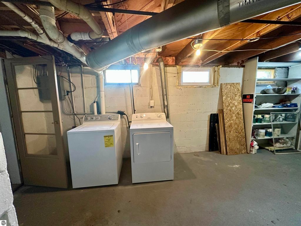 Basement laundry area featuring a washing machine and dryer, with well-lit windows and organized storage shelves, highlighting the clean and dry condition of the space at 209 W Fifteenth Street, Traverse City, MI.