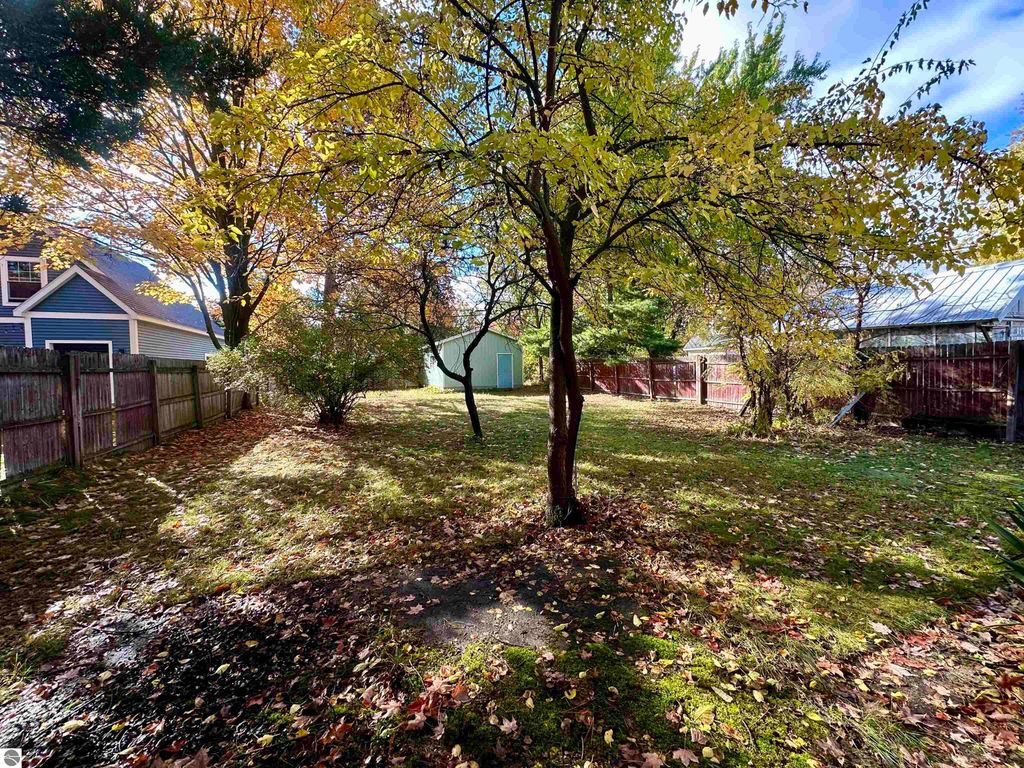 Backyard view of residential property at 209 W Fifteenth Street, Traverse City, featuring autumn foliage, fenced yard, and garage in background.