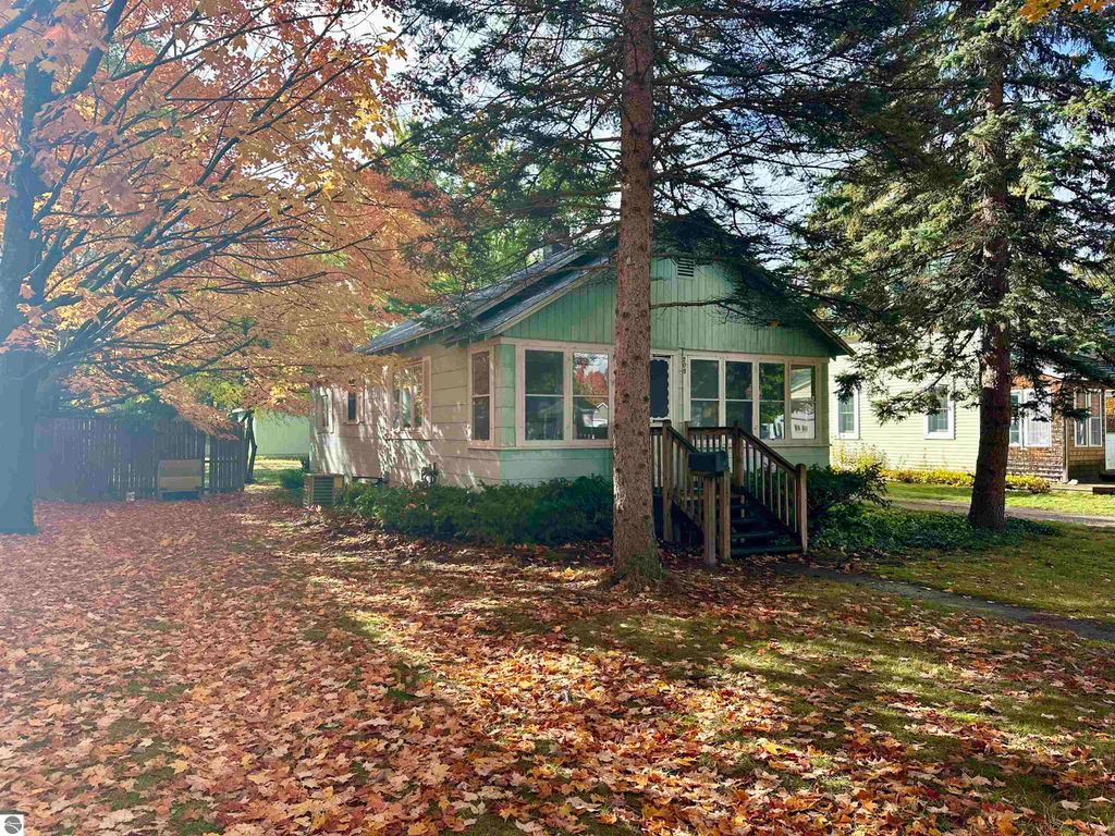 Charming residential property at 209 W Fifteenth Street, Traverse City, surrounded by autumn foliage, featuring an enclosed front porch and a tree-lined yard.