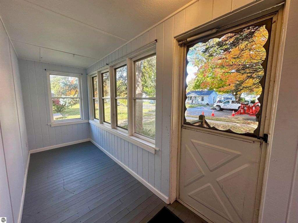 Enclosed front porch of a one-bedroom home at 209 W Fifteenth Street, Traverse City, featuring light blue walls, large windows, and a view of autumn foliage outside.